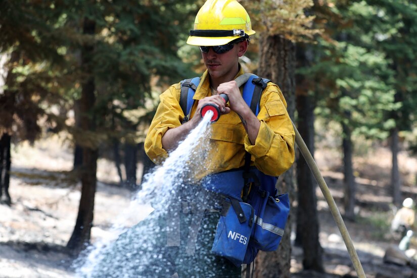 A soldier sprays water from a hose in a wooded area.