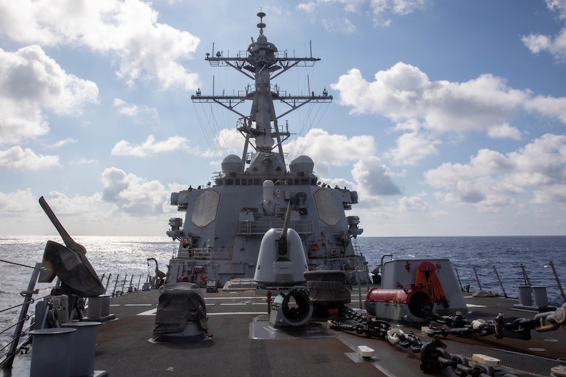 Large guns and equipment adorn the deck of a ship at sail.