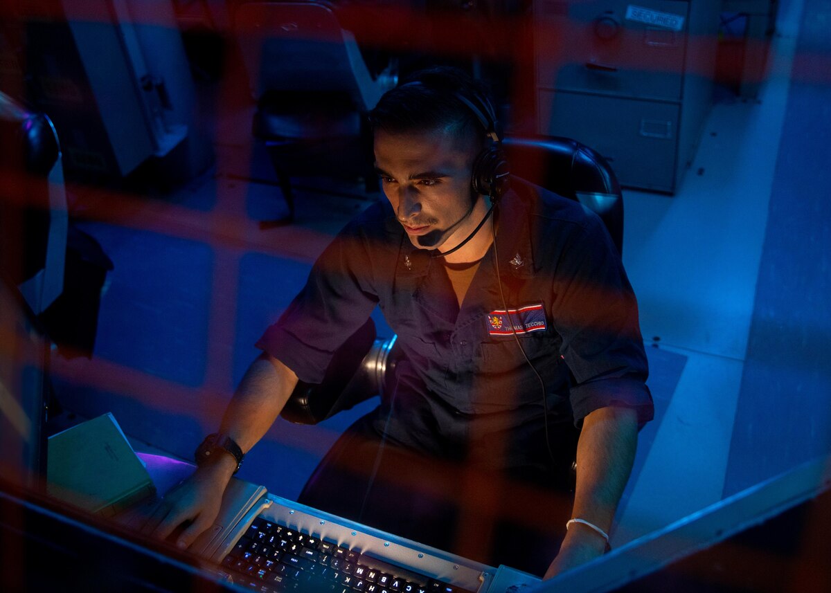 A man wearing a headset sits behind a computer.