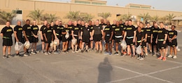 35 men and women stand in black shorts and shirts with yellow writing. Some hold plastic trashbags.