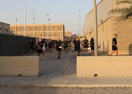 36 individuals in black shorts and black t-shirts with yellow lettering walk down a path picking up trash