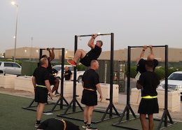 three Soldiers in black shorts and t-shirt observe three soldiers in black shorts and t-shirt on a pull up bar tucking their legs to their elbows.