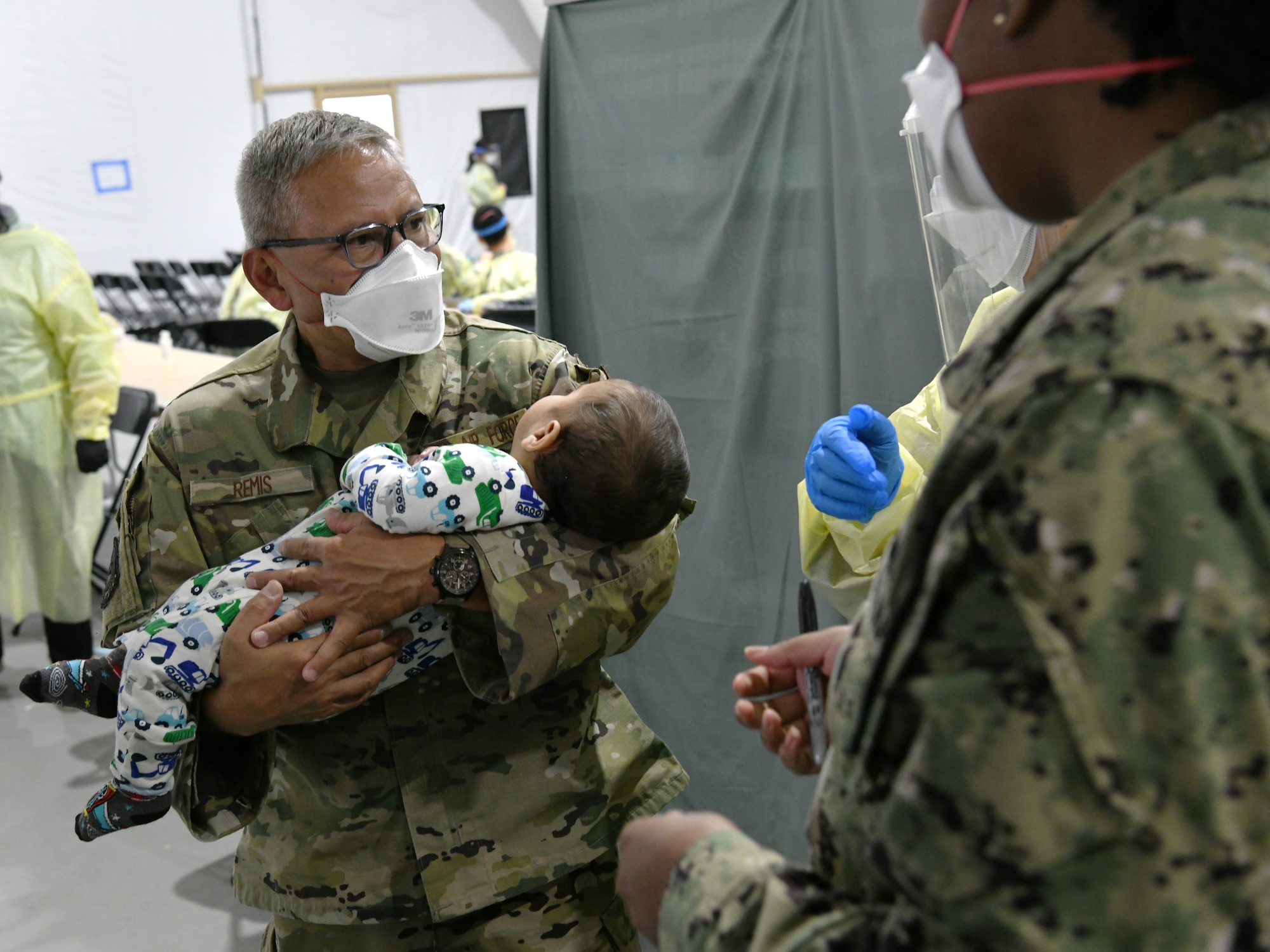 Washington Air National Guard Master Sgt. Andy Remis, assigned to the 116th Air Support Operations Squadron, Camp Murray, Wash., lends a helping hand, holding an Afghan child at the Task Force Liberty Village medical station, Joint Base McGuire-Dix-Lakehurst, New Jersey, Sept. 11, 2021.  The Department of Defense, through U.S. Northern Command, and in support of the Department of Homeland Security, is providing transportation, temporary housing, medical screening, and general support for at least 50,000 Afghan evacuees at suitable facilities, in permanent or temporary structures, as quickly as possible. This initiative provides Afghan personnel essential support at secure locations outside Afghanistan. (National Guard photo by Master Sgt. John Hughel, Washington Air National Guard)