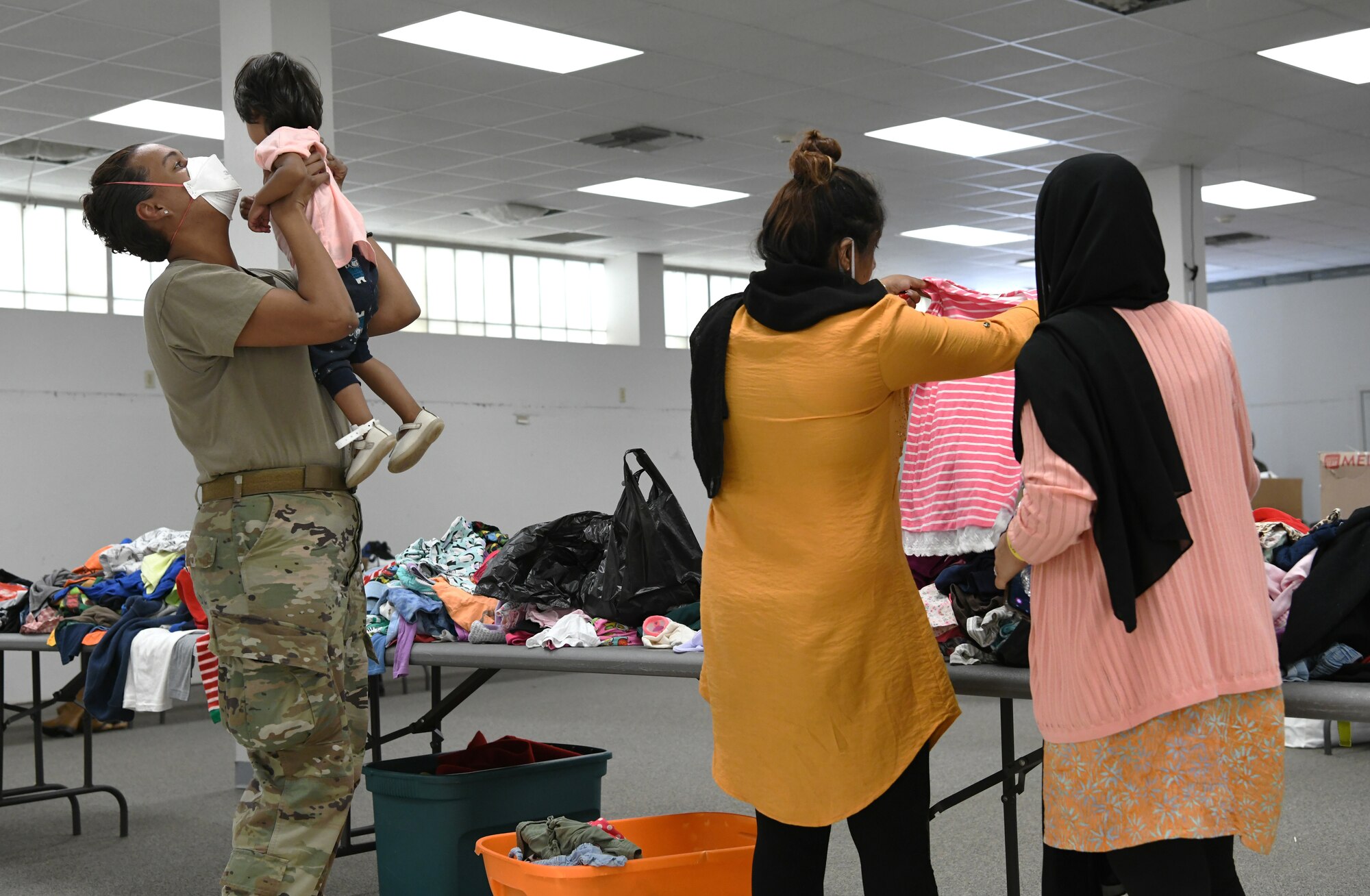 U.S. Air Force Senior Airman Sarina Crowder, Task Force Liberty personnel from 4th Medical Group at Seymour Johnson Air Force Base, North Carolina, holds a young Afghan girl while her mother looks for clothing at Liberty Village on Joint Base McGuire-Dix-Lakehurst, New Jersey, Sept. 2, 2021. The Department of Defense, through U.S. Northern Command, and in support of the Department of Homeland Security, is providing transportation, temporary housing, medical screening, and general support for at least 50,000 Afghan evacuees at suitable facilities, in permanent or temporary structures, as quickly as possible. This initiative provides Afghan personnel essential support at secure locations outside Afghanistan. (National Guard photo by Master Sgt. John Hughel, Washington Air National Guard)