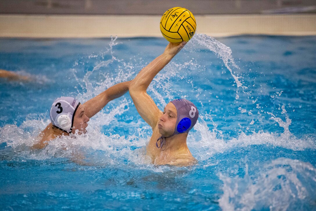 An airman prepares to pass a ball during a water polo match in a swimming pool.