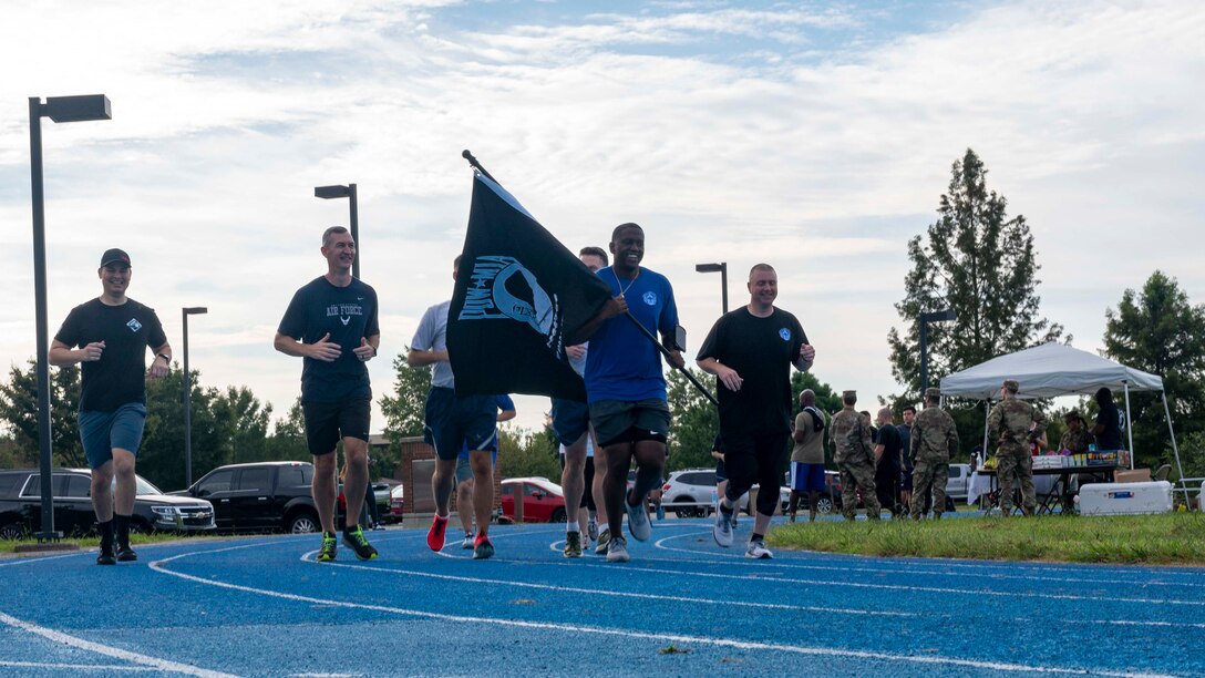 Service members run with the POW/MIA flag.