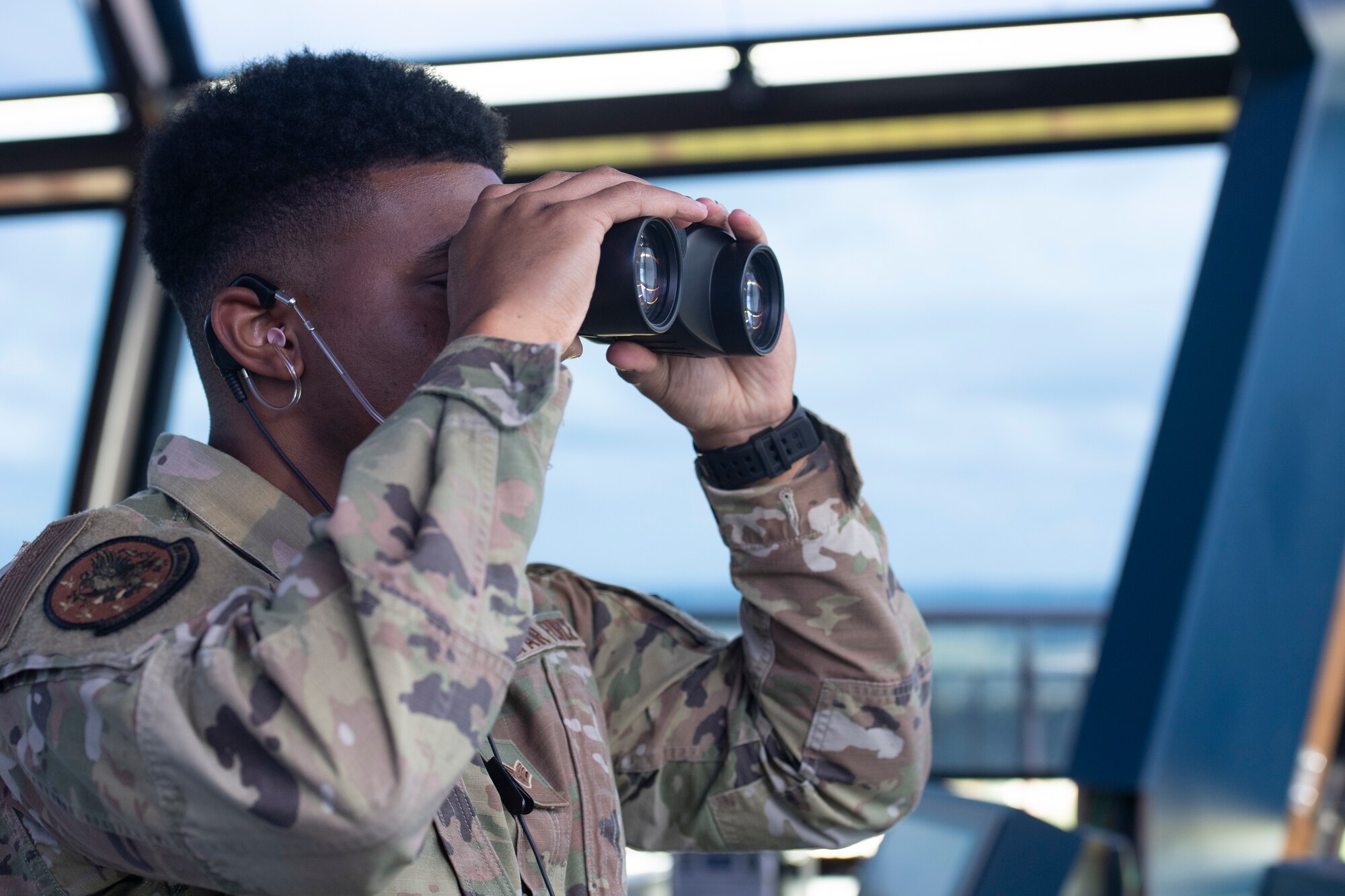 U.S. Air Force Senior Airman Raymond Fields, 52nd Operations Support Squadron air traffic control specialist, peers through his binoculars as a commercial airliner taxis onto the Spangdahlem Air Base runway at Spangdahlem Air Base, Germany, Aug. 23, 2021.