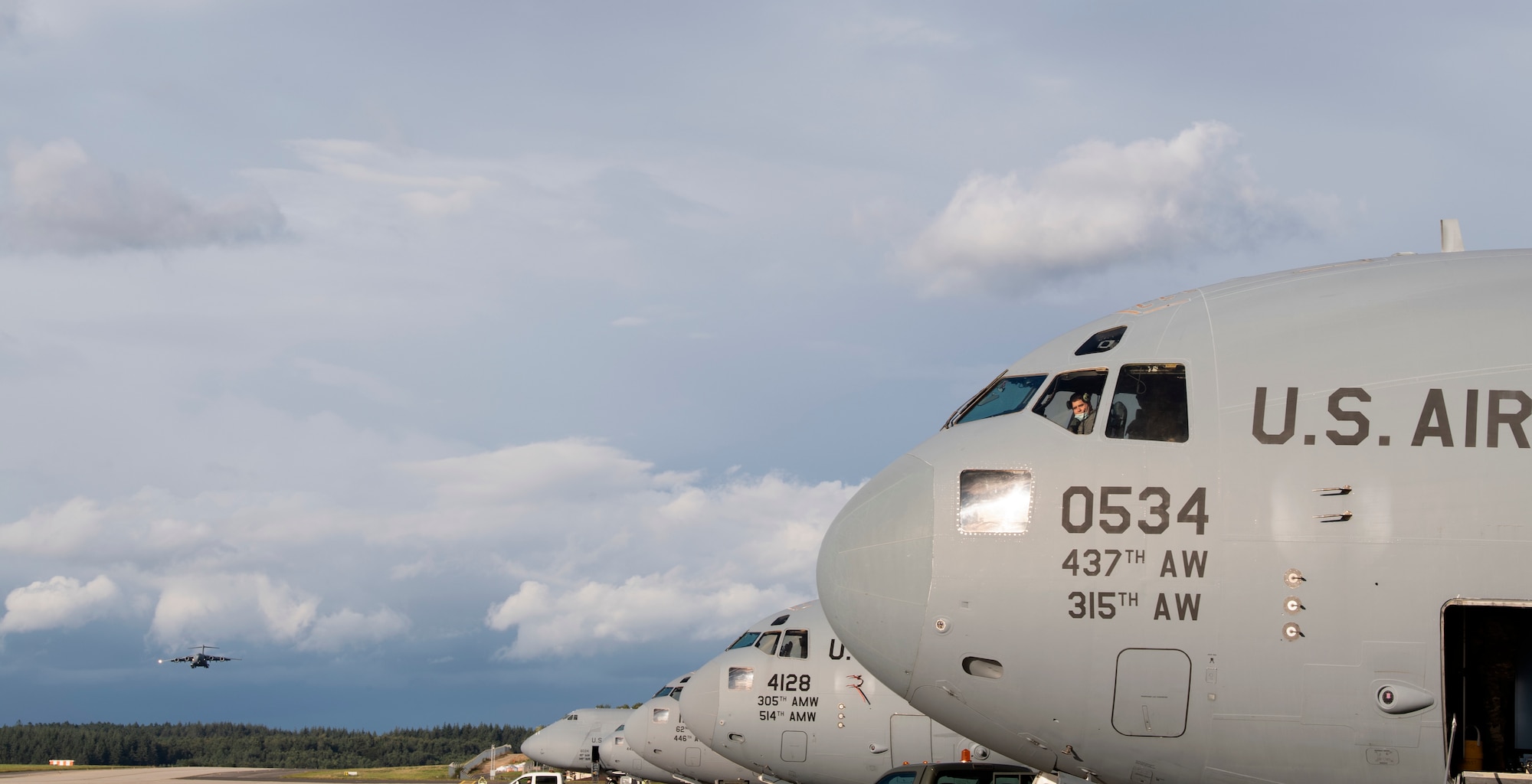 A U.S. Air Force C-17 Globemaster III assigned to Joint Base Charleston, South Carolina, prepares to land on the flightline of Spangdahlem Air Base, Germany, near a row of parked Air Mobility Command cargo aircraft Aug. 27, 2021.