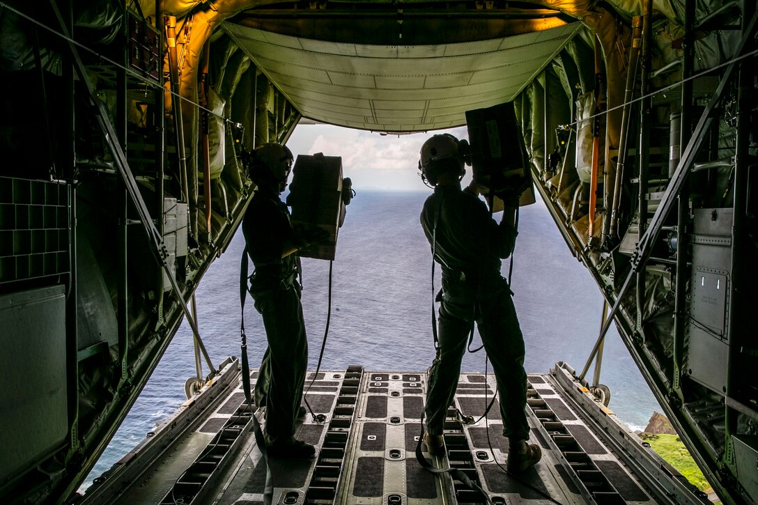 Marines prepare to throw cargo out of the back of an airborne aircraft.
