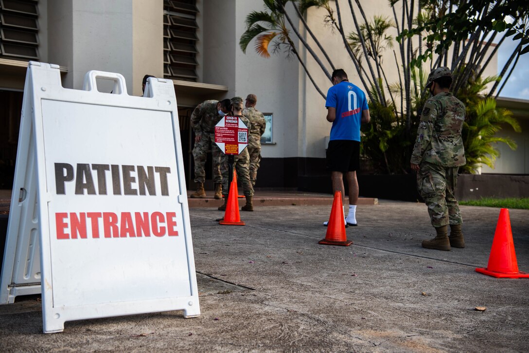 Several service members stand in line. A sign saying “patient entrance” is in the foreground.