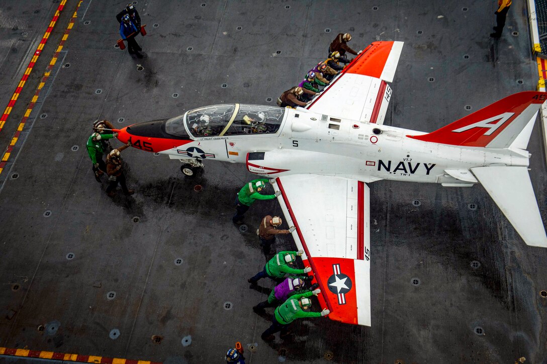 Sailors seen from overhead push an aircraft on a ship's deck.