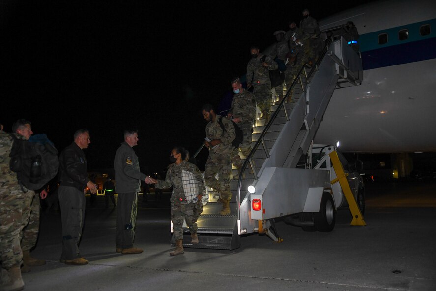 Airmen descend aircraft stairs to shake hands with the 5th Bomb Wing commander