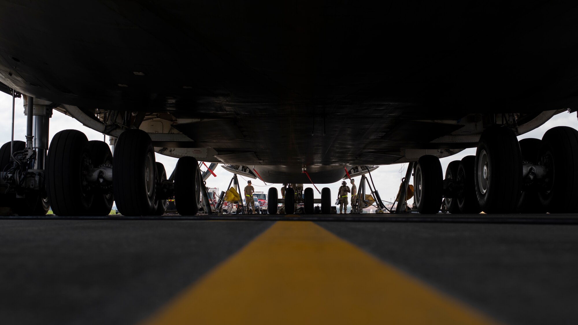 The underside of a very large cargo plane with several maintainer Airmen peering underneath from the far end