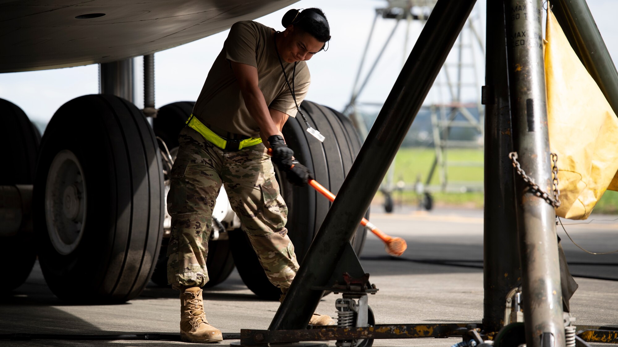 An Airman with a long hammer pounds into place a large airplane jack