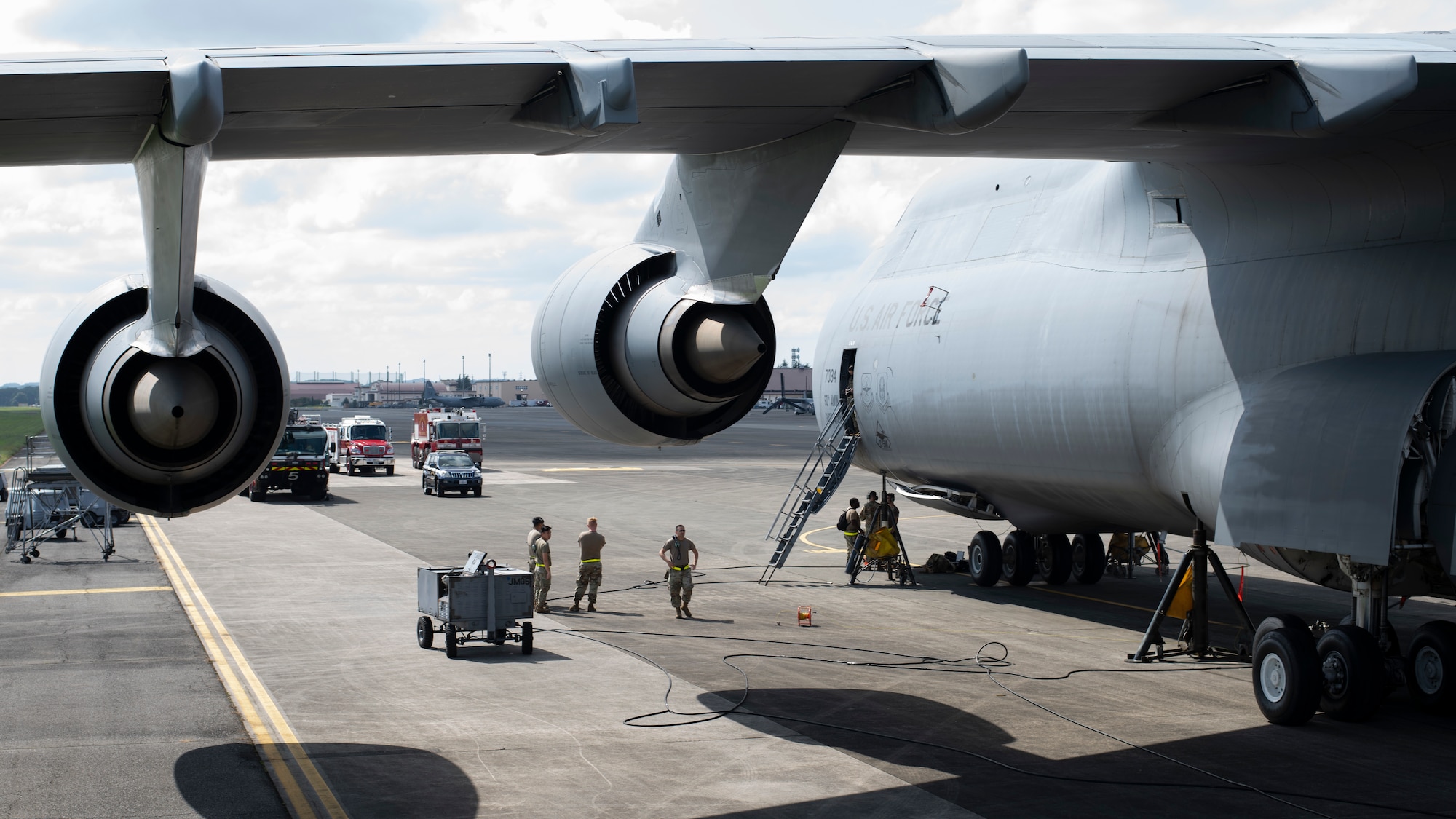 Wide side-view of a very large cargo plane with three red fire trucks in the in-front of it