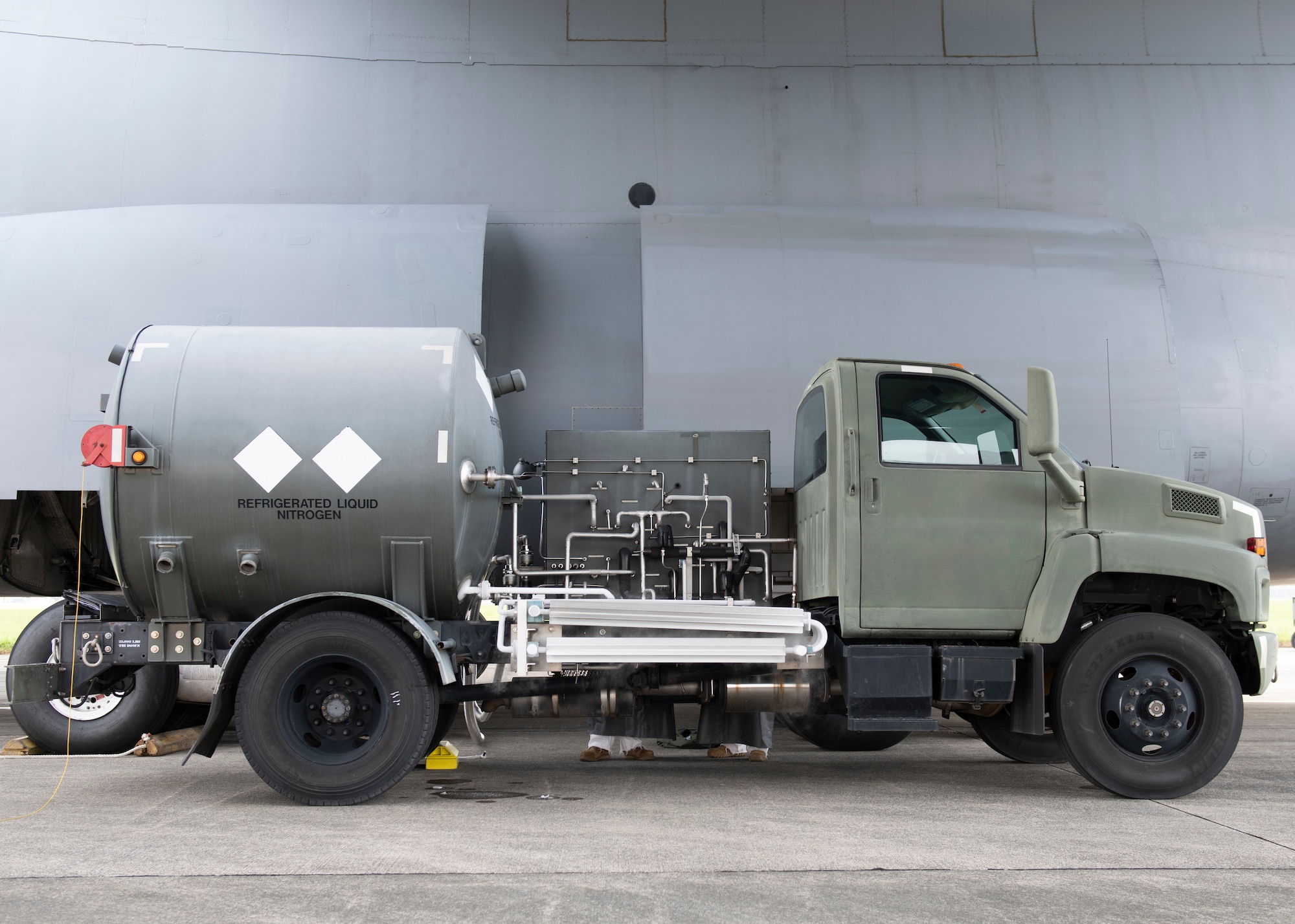 A utility truck with a large tank on the back is parked next to a much larger cargo plane