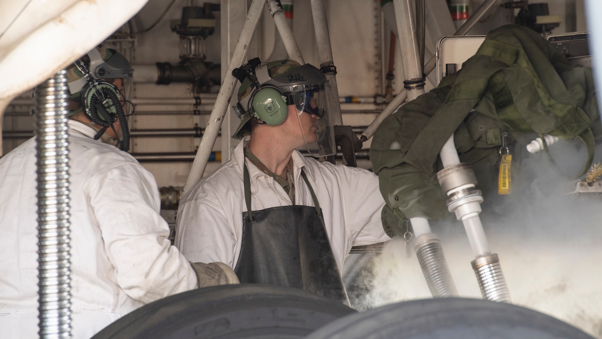 Two Airmen in white coveralls and protective face shields refilling a nitrogen tank