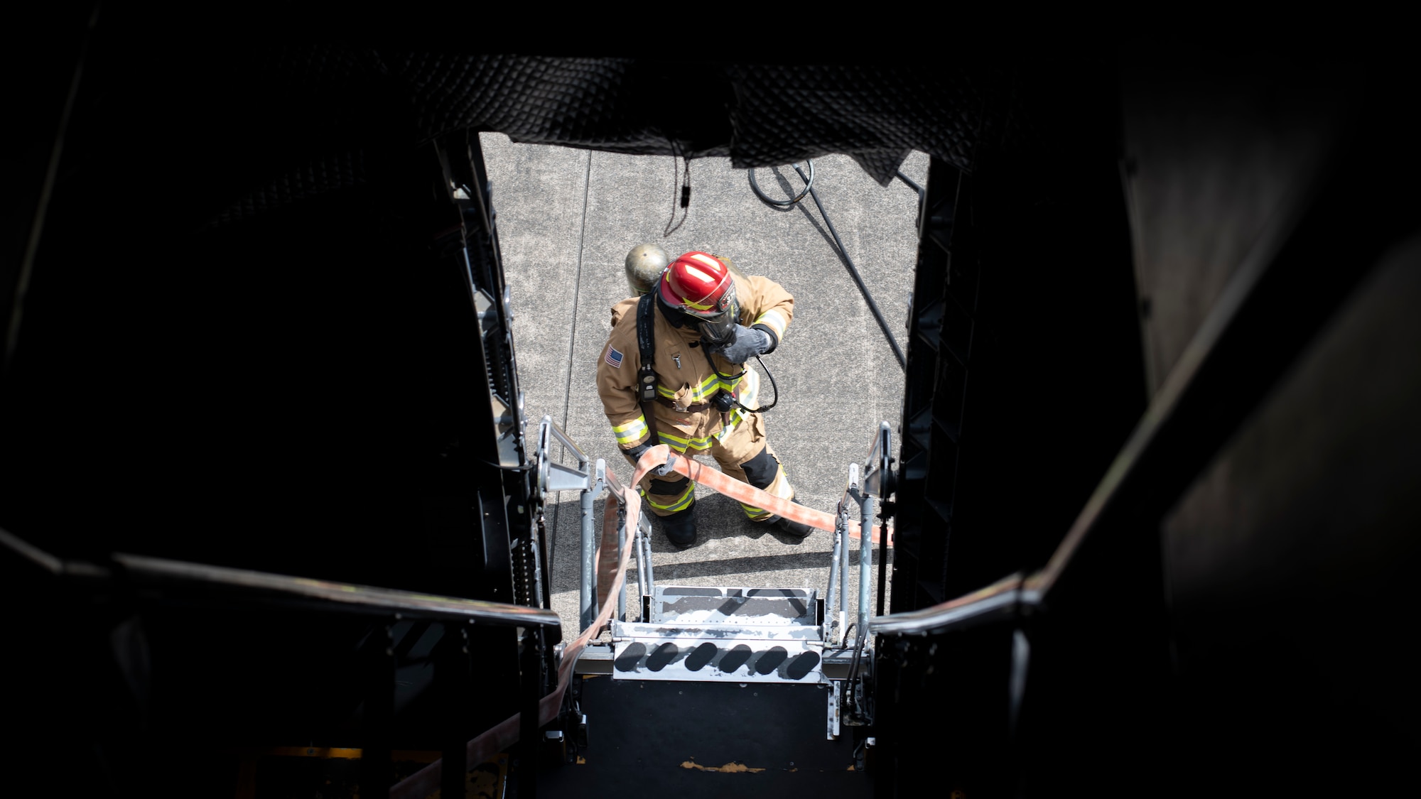 A firefighter carrying a fire hose is framed in the dark entry hatch of a very large cargo plane