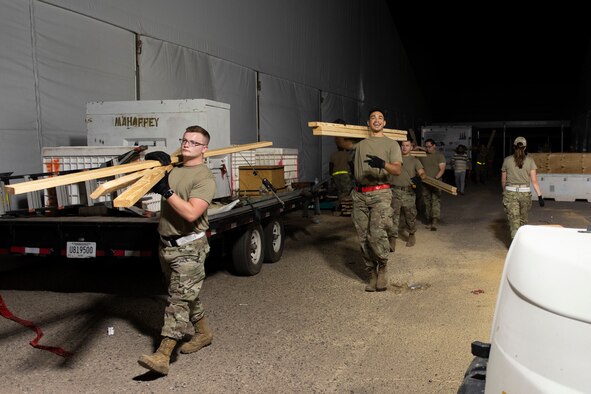 Airmen from Task Force-Holloman carry wood to build partitions for Afghan evacuee living quarters at Holloman Air Force Base, New Mexico, Sept. 4, 2021. The Department of Defense, through U.S. Northern Command, and in support of the Department of State and Department of Homeland Security, is providing transportation, temporary housing, medical screening, and general support for at least 50,000 Afghan evacuees at suitable facilities, in permanent or temporary structures, as quickly as possible. This initiative provides Afghan evacuees essential support at secure locations outside Afghanistan. (U.S. Air Force photo by Staff Sgt. Kenneth Boyton)
