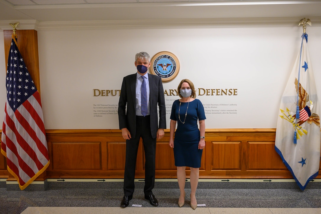 A man and a woman stand in a lobby. The signage on the wall behind them indicates that they are at the Department of Defense.