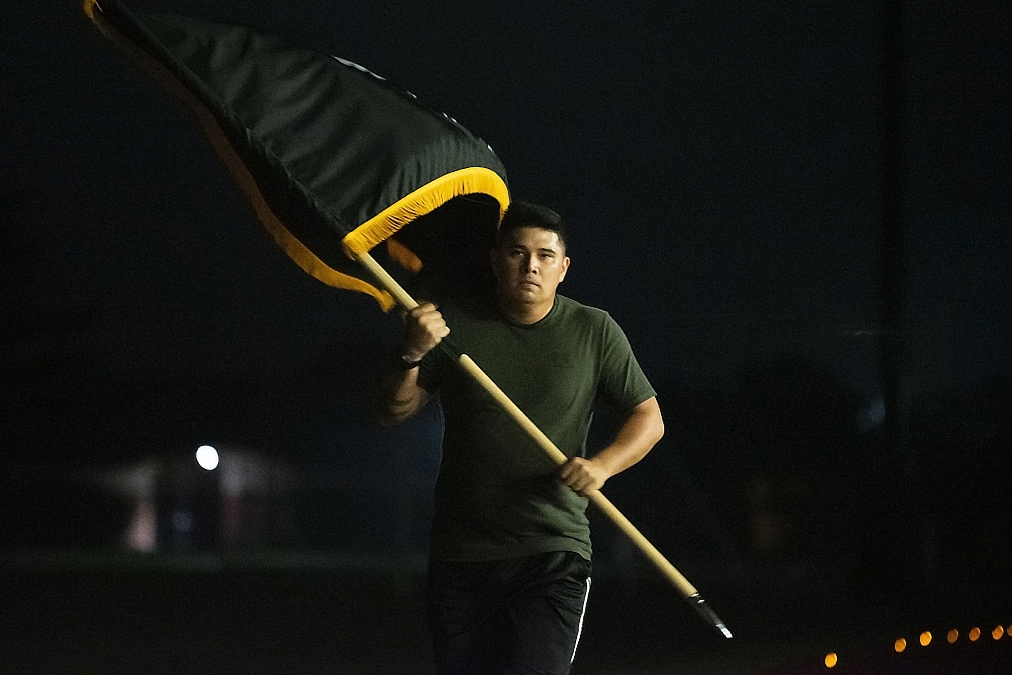 Airman runs around the gym track with the POW/MIA flag, at night.