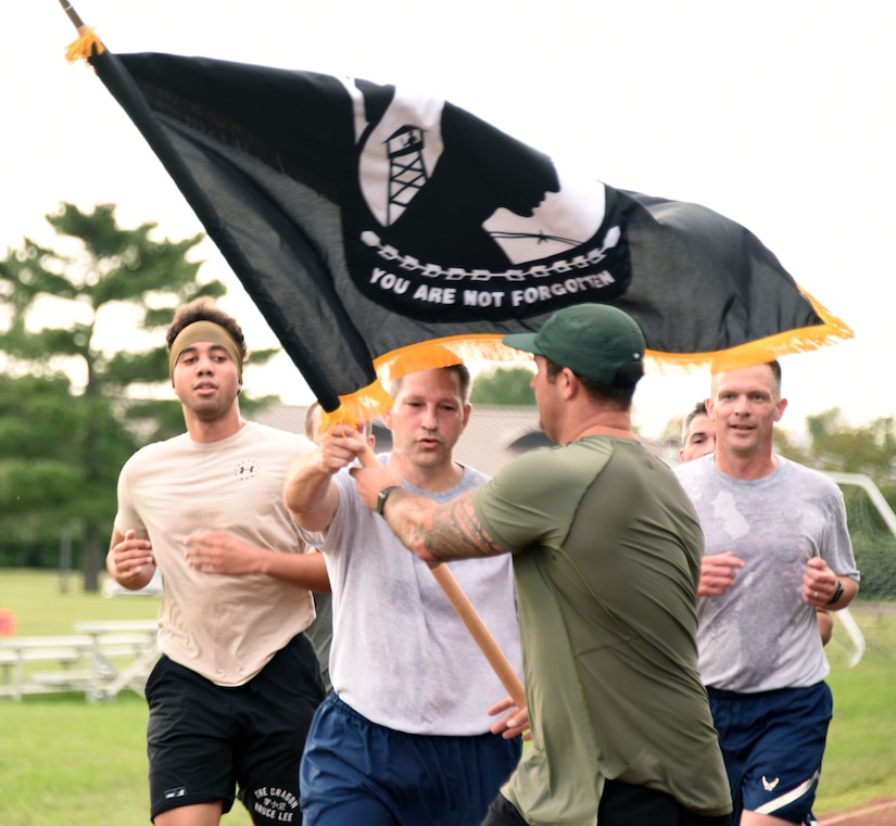 305th AMW participant hands over POW/MIA flag to emergency response team member while running around the gym track.
