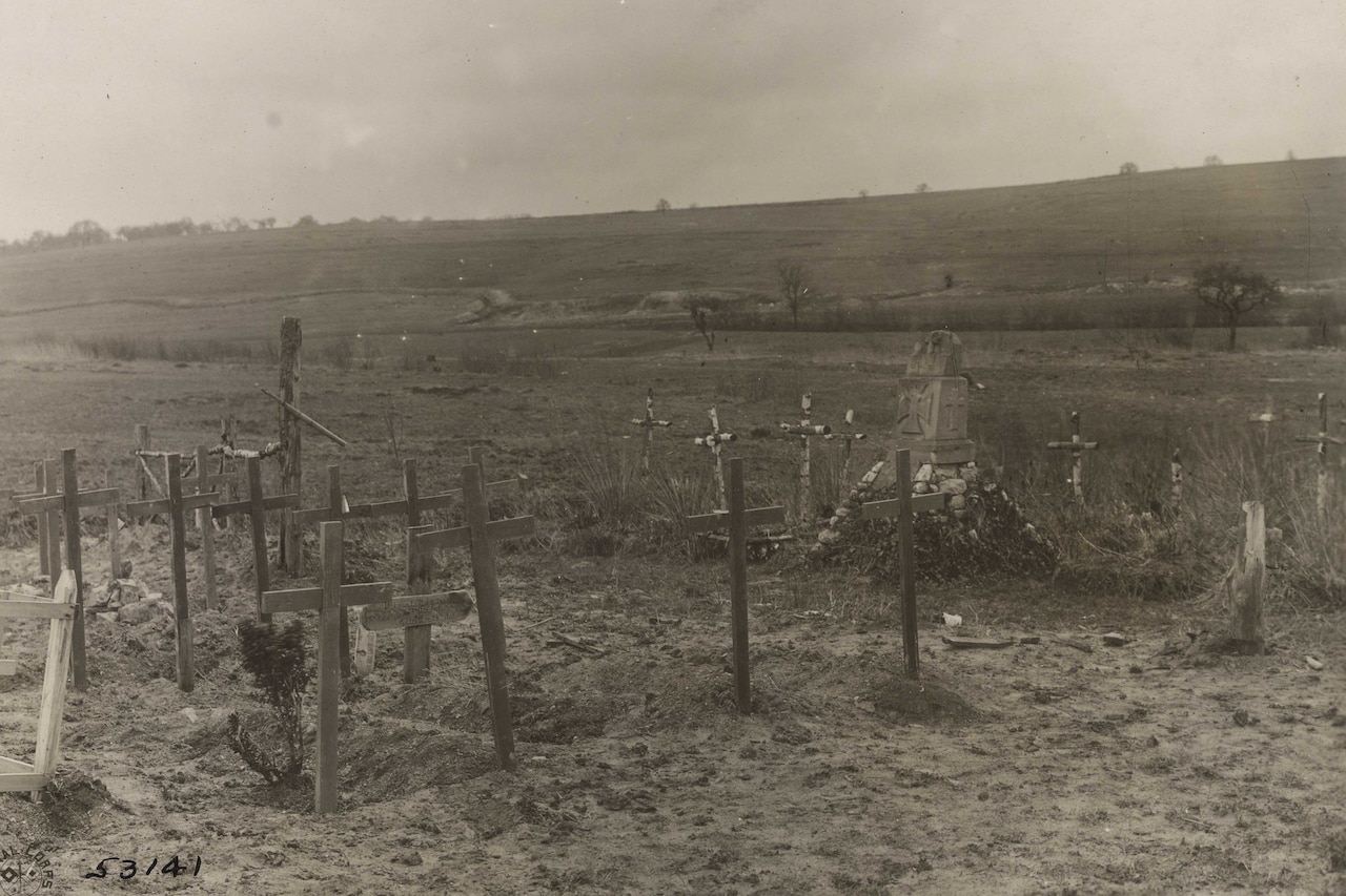 Several crosses mark gravesites over barren flat land.