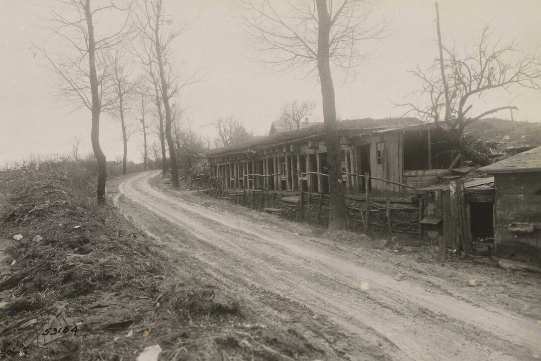 A wooden building sits behind a wooden fence alongside a dirt road.