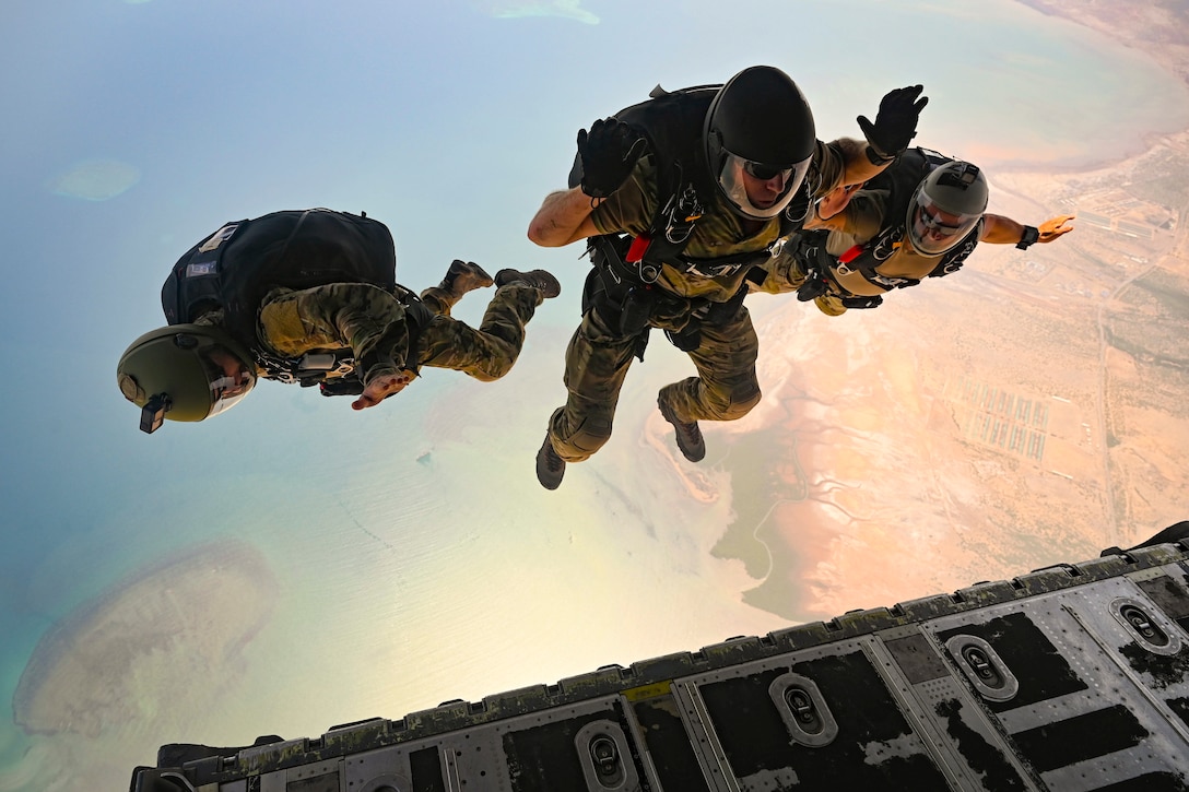Three airmen freefall after jumping from an aircraft wearing parachute gear.