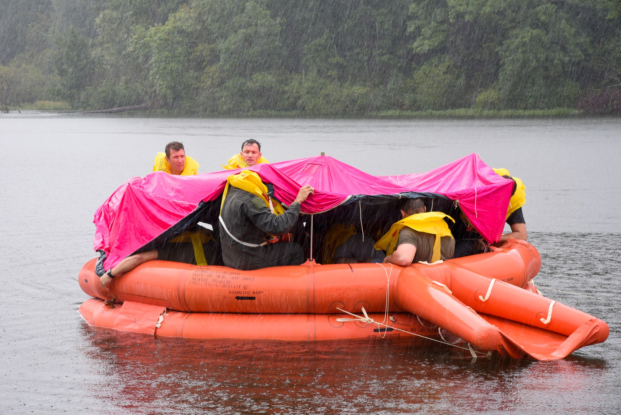Airmen put a tarp over a raft during water survival training.