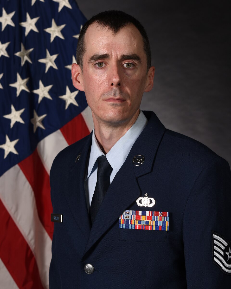 An Airman in uniform posed in front of a flag