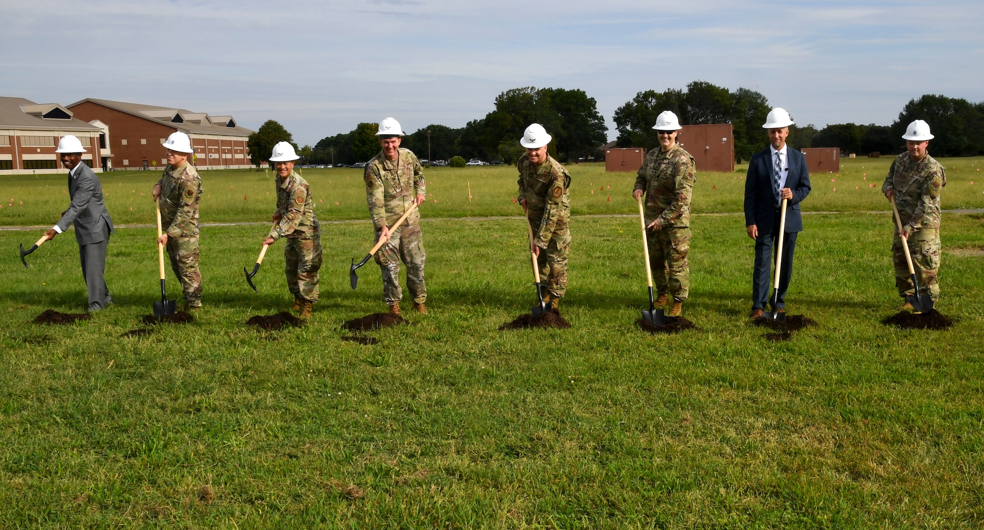 Eight individuals shovel a pile of dirt.