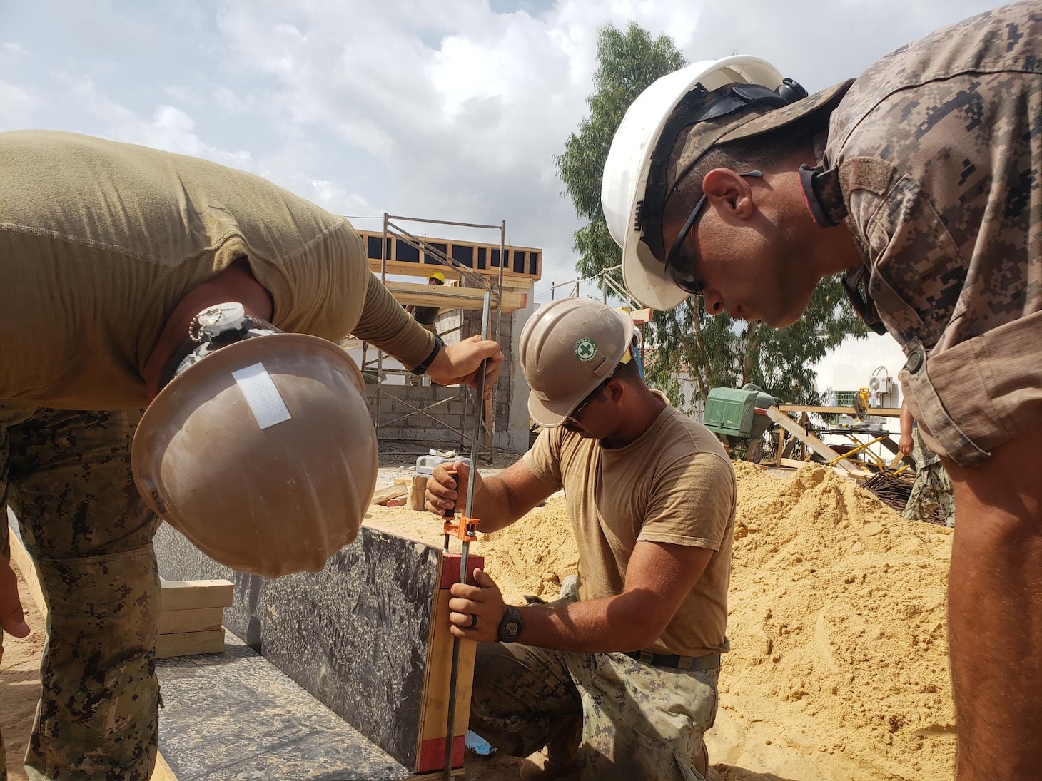 Steelworker Constructionman Rusty Garza and Builder Constructionman Kai Zanjanipour from NMCB 11 work with First Soldier Daji Oussama of the Tunisian Engineers to set concrete formwork for the building foundation.