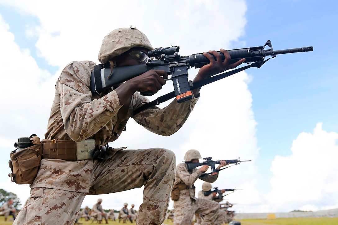 Marine Corps recruits point weapons while kneeling on the ground.