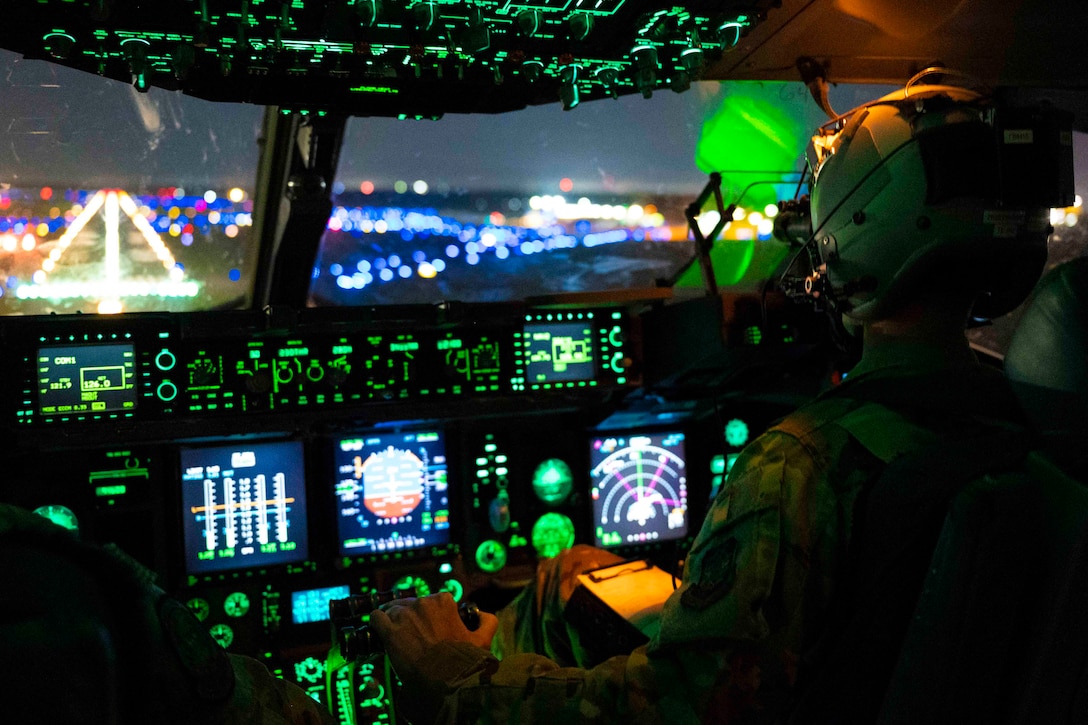 An airman sits in the cockpit of an airborne aircraft at night.