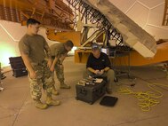 Two U.S. Airmen stand and man sits working on computer