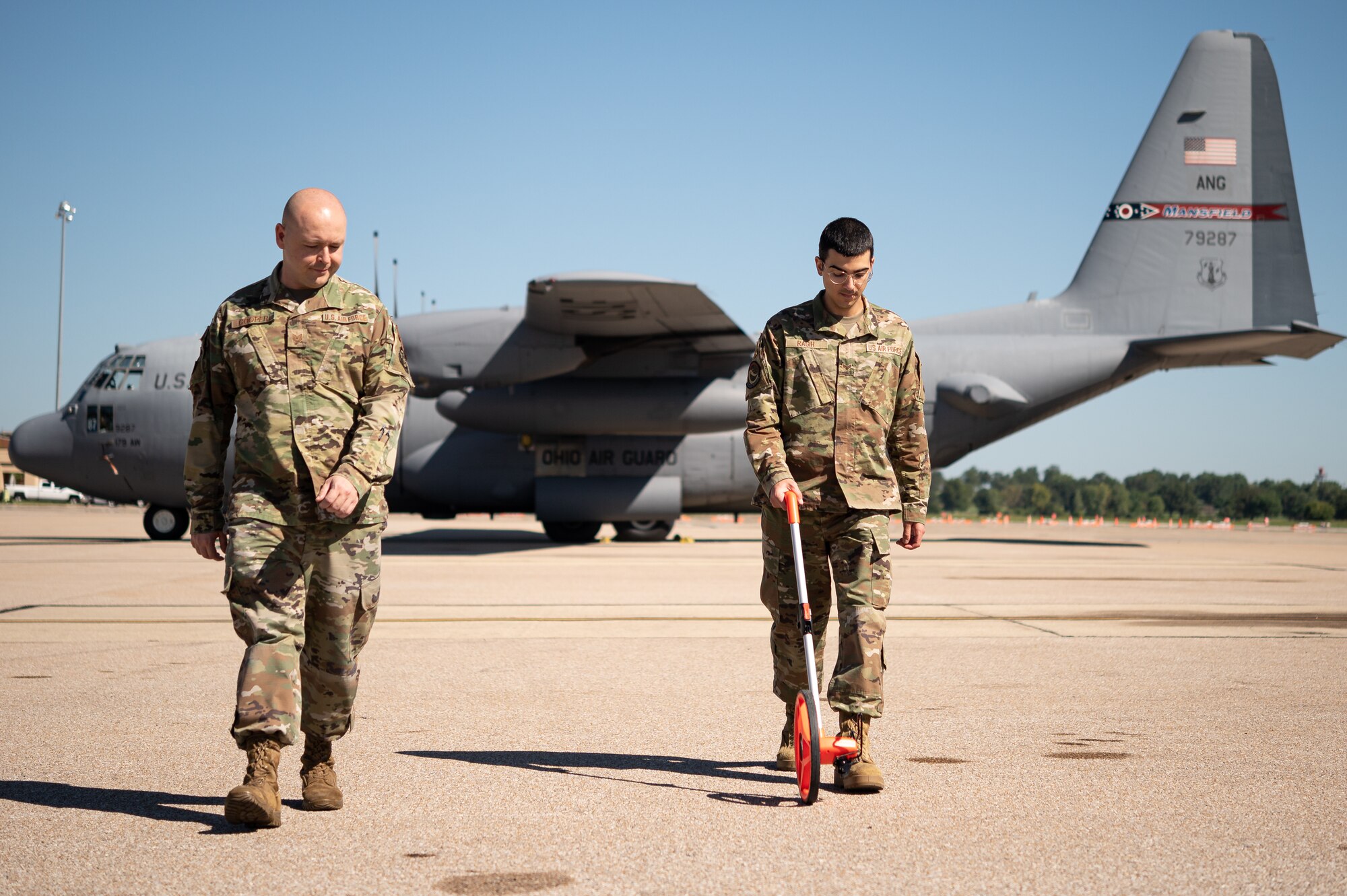 U.S. Air Force Senior Airman Samir Ragih, 375th Operation Support Squadron airfield management shift lead, and Tech. Sgt. Anthony Cooper, 375th OSS NCOIC of airflow manager operations, measure the distance between two C-130 on Scott Air Force Base, Illinois Sept. 8, 2021. The airfield management Airmen ensure that the Aircraft are properly placed to ensure that they utilize their space, while keeping the mission safe.(U.S. Air Force Photo by Airman 1st Class Isaac Olivera)
