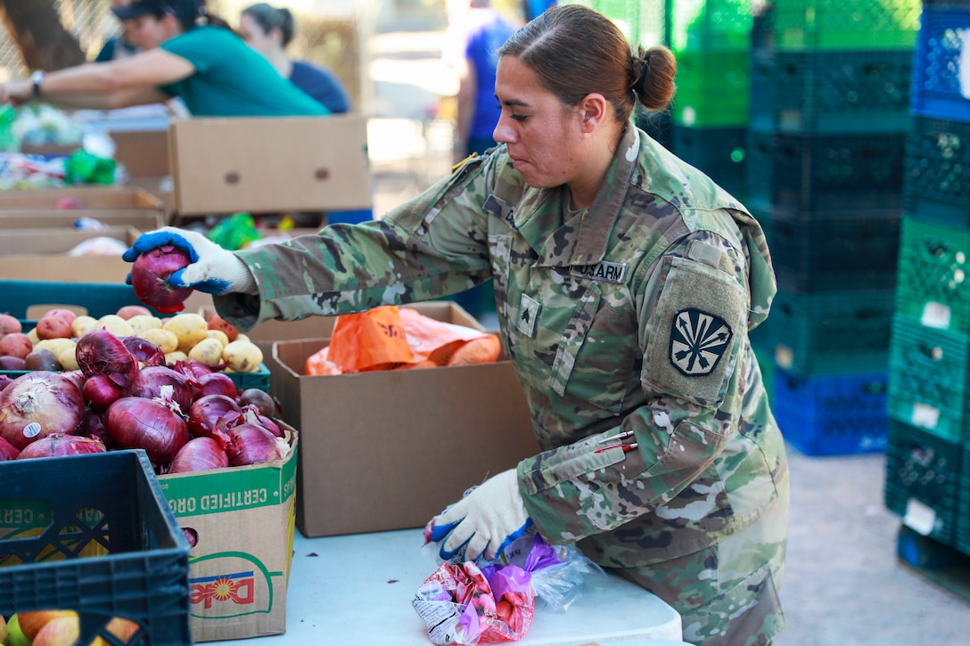 A soldier wearing gloves prepare boxes of groceries for area residents.