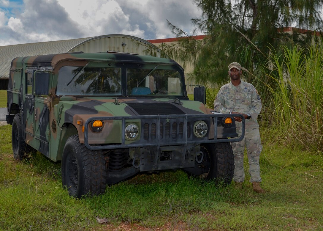 A member of the U.S. Space Force in a camouflaged uniform stands next to a Humvee in a tropical setting.