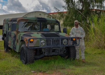 A member of the U.S. Space Force in a camouflaged uniform stands next to a Humvee in a tropical setting.