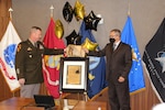 A soldier in Army dress greens stands to the left as he and a man in business attire jointly unveil a ceremonial image with flags of the United States and its military services in the background.