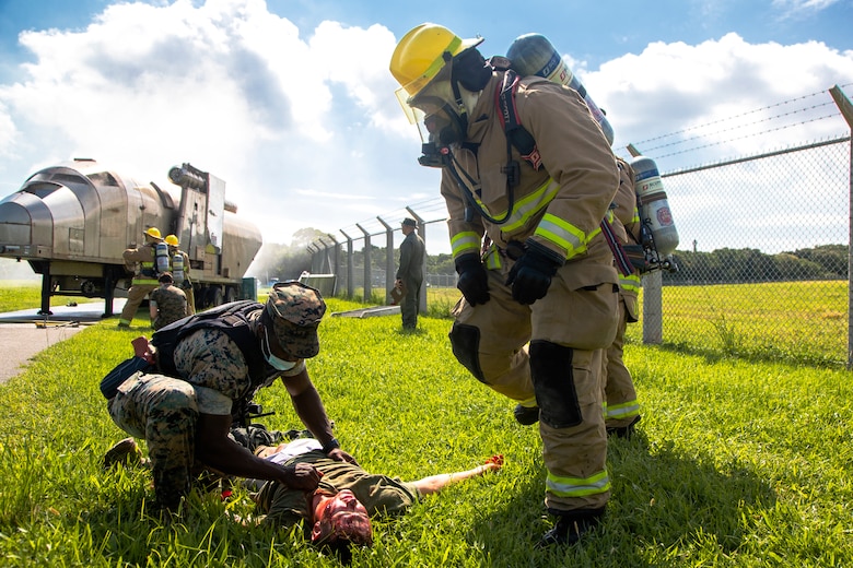 U.S. Marine Corps Cpl. Jason Joseph, foreground left, a military police officer with the Marine Corps Air Station (MCAS) Futenma Provost Marshal Office, Marine Corps Installations Pacific (MCIPAC) – Marine Corps Base Camp Butler, triages a simulated casualty as Marines with the MCAS Futenma Expeditionary Crash, Fire and Rescue, Headquarters and Headquarters Squadron, MCAS Futenma, MCIPAC, prepare to transport the patient to safety during an aircraft mishap drill near Gate 3 of MCAS Futenma, Okinawa, Japan, Sept. 21, 2021. The scenario was the signature event of Constant Vigilance 2021 on the air station and served to ensure MCAS Futenma and its personnel are able to respond to crises at a moment's notice. (U.S. Marine Corps photo by Cpl. Ryan H. Pulliam)