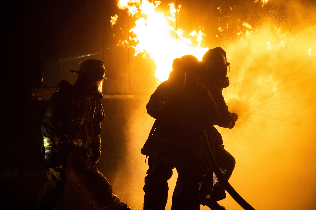 Marines are silhouetted against a blazing fire.