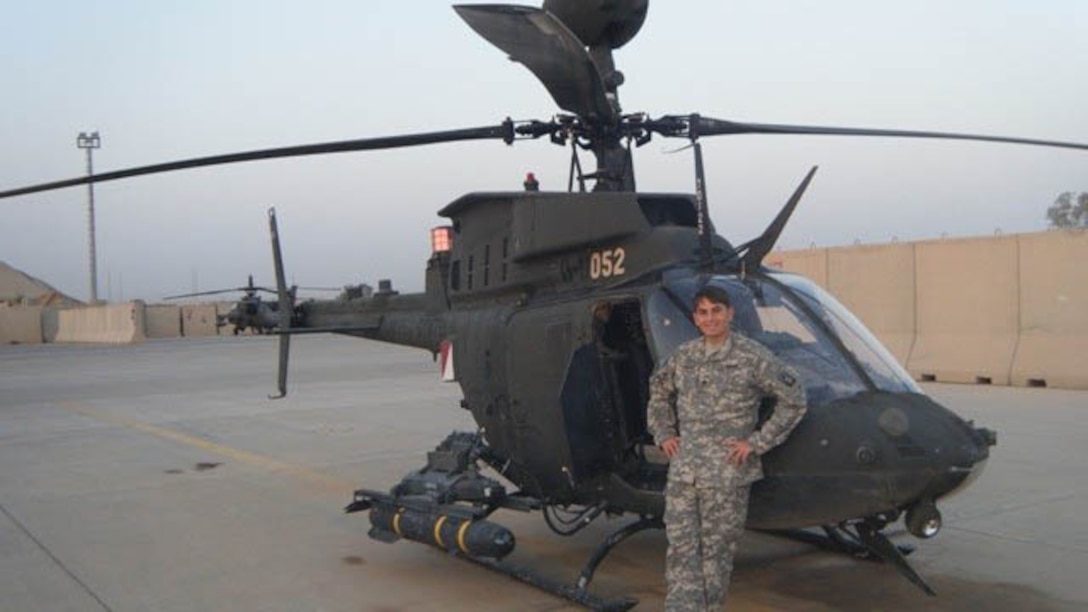 Army Chief Warrant Officer 3 José Miguel Sánchez López poses next to a OH-58D Kiowa Warrior Scout helicopter.
