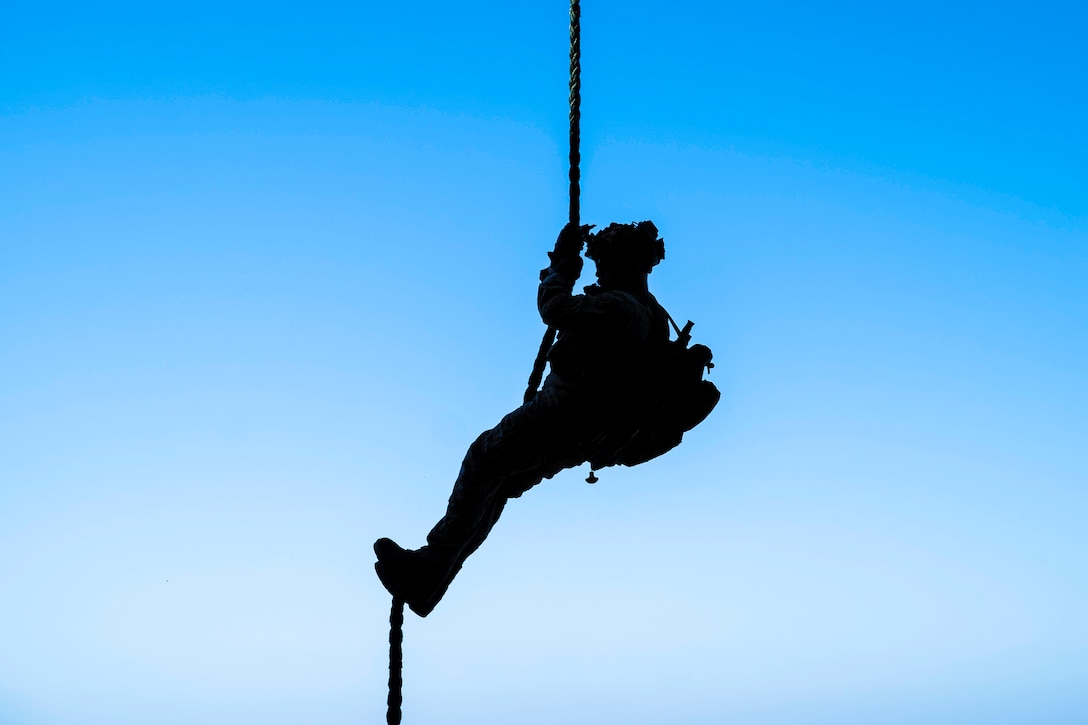 A Marine shown in silhouette moves down a rope.