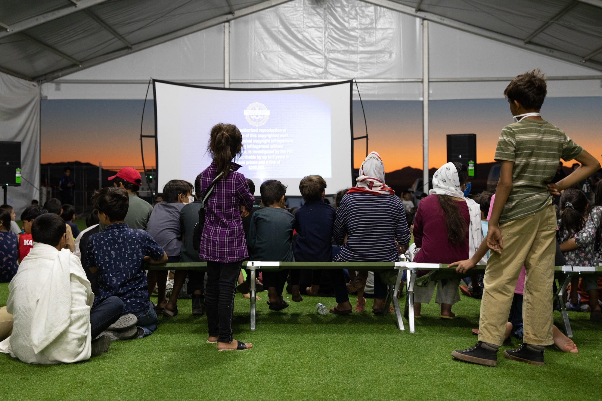 Afghan evacuees get ready to watch a movie set up by the Department of Homeland Security as a recreational activity in support of Operation Allies Welcome on Holloman Air Force Base, New Mexico, Sept. 20, 2021. The Department of Defense, through the U.S. Northern Command, and in support of the Department of State and Department of Homeland Security, is providing transportation, temporary housing, medical screening, and general support for at least 50,000 Afghan evacuees at suitable facilities, in permanent or temporary structures, as quickly as possible. This initiative provides Afghan evacuees essential support at secure locations outside Afghanistan. (U.S. Army photo by Spc. Nicholas Goodman)