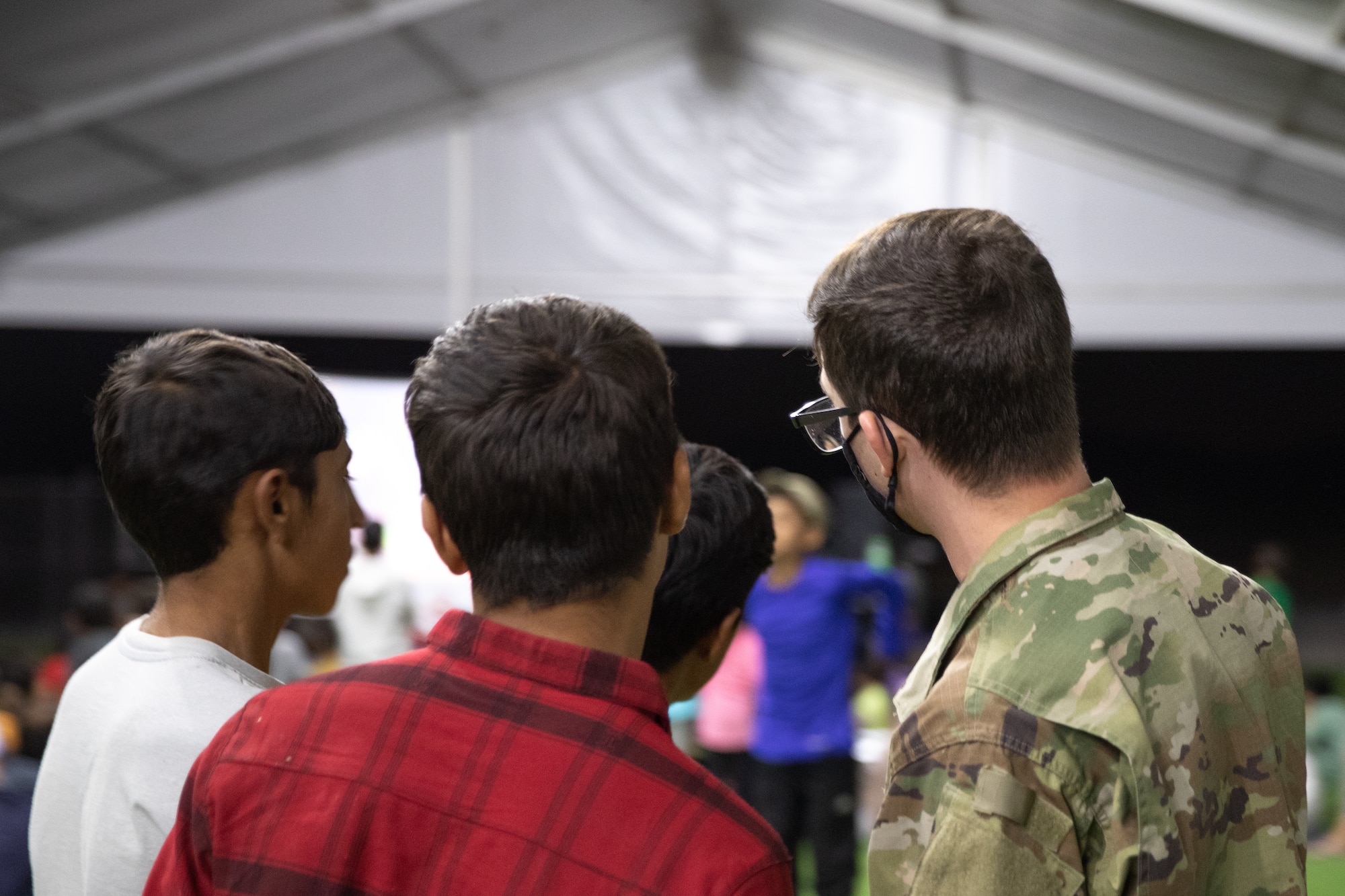 An Airman interacts with Afghan evacuees as part of a movie night set up by the Department of Homeland Security as a recreational activity in support of Operation Allies Welcome on Holloman Air Force Base, New Mexico, Sept. 20, 2021. The Department of Defense, through the U.S. Northern Command, and in support of the Department of State and Department of Homeland Security, is providing transportation, temporary housing, medical screening, and general support for at least 50,000 Afghan evacuees at suitable facilities, in permanent or temporary structures, as quickly as possible. This initiative provides Afghan evacuees essential support at secure locations outside Afghanistan. (U.S. Army photo by Spc. Nicholas Goodman)