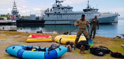 Jamaican service member on shore with survival equipment and ships in background.