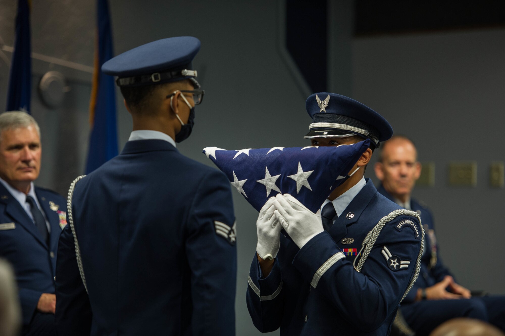 Base Honor Guard airman hands a folded American flag to another Honor Guard member.