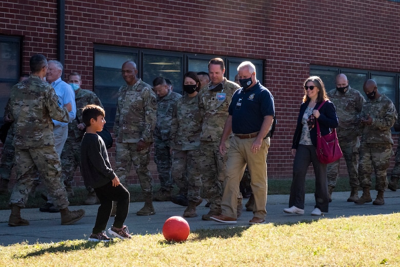 Secretary of the Air Force Frank Kenall, Chief of Staff of the Air Force Gen. CQ Brown, Jr. and Chief Master Sergeant of the Air Force JoAnne Bass pass by an Afghan child playing soccer inside of Liberty Village on Joint Base McGuire-Dix-Lakehurst, New Jersey, Sept. 25, 2021. The Department of Defense, through U.S. Northern Command, and in support of the Department of Homeland Security, is providing transportation, temporary housing, medical screening, and general support for at least 50,000 Afghan evacuees at suitable facilities, in permanent or temporary structures, as quickly as possible. This initiative provides Afghan personnel essential support at secure locations outside Afghanistan. (U.S. Air Force photo by Staff Sgt. Jake Carter)